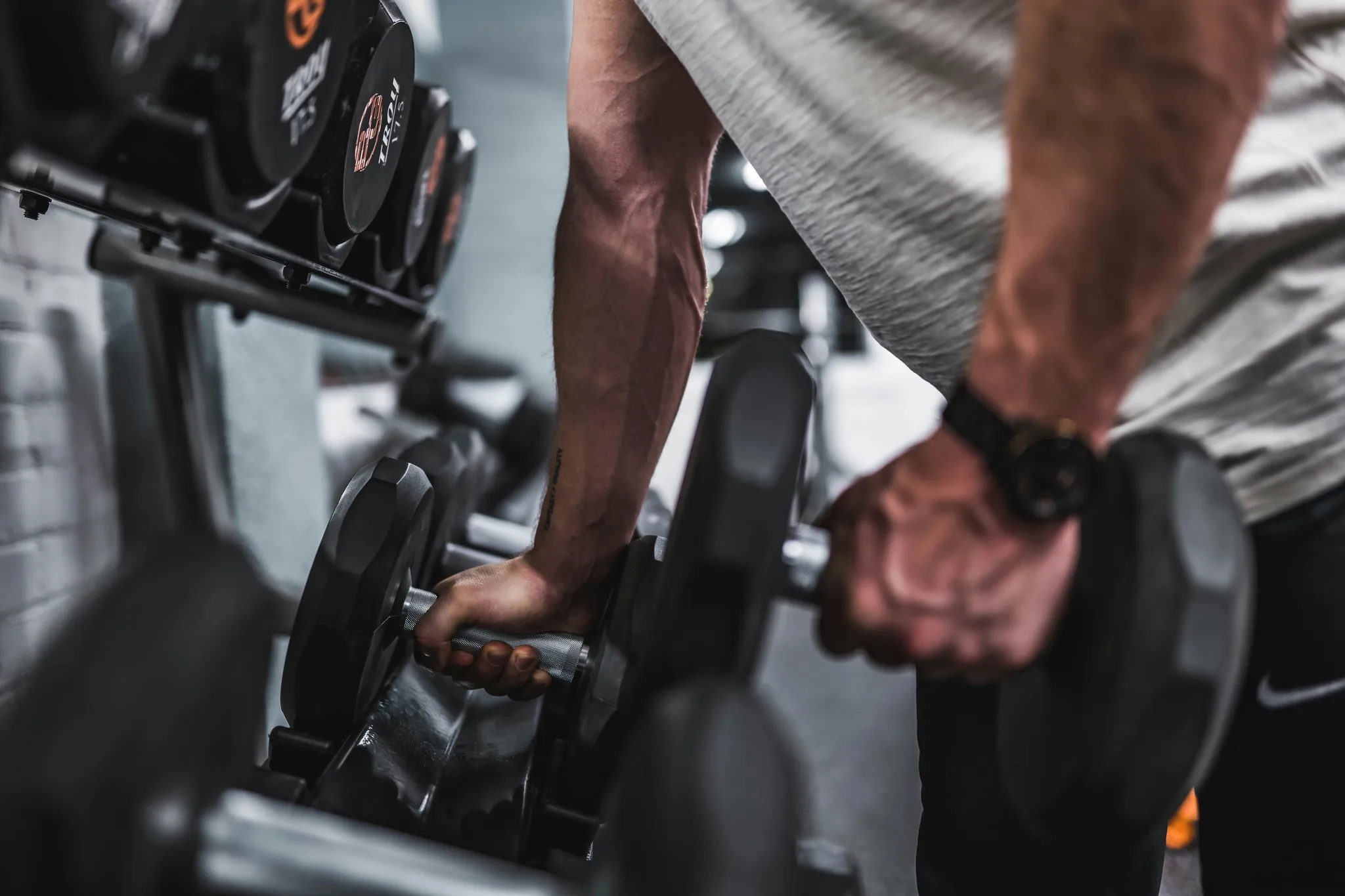 Man selecting dumbbells from a rack in a gym